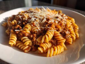 A close-up of a white bowl filled with creamy beef pasta (rotini) topped with shredded Parmesan cheese.