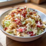 A close-up of creamy BLT pasta salad featuring rotini pasta, cherry tomatoes, lettuce, and bacon crumbles.