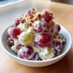 Close-up of creamy chicken salad chick grape salad mixture with red and green grapes coated in dressing and topped with pecans.