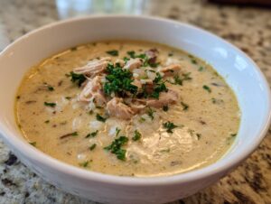 Close-up of a creamy chicken wild rice soup topped with shredded chicken and fresh parsley.
