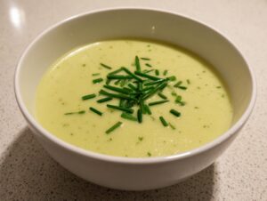 A close-up of a bowl of smooth, pale green leek soup topped with freshly chopped chives.