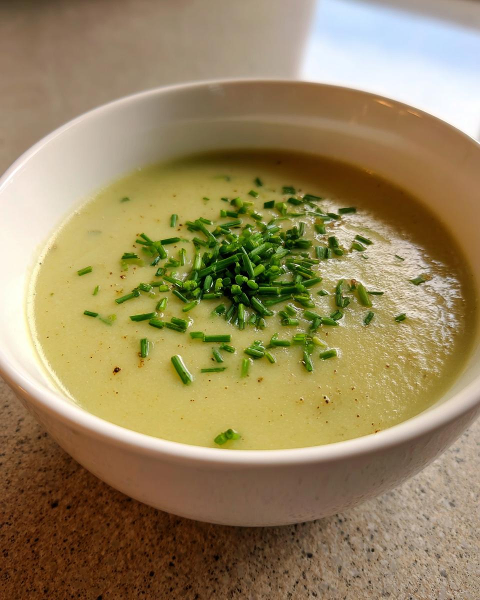 Close-up of a bowl of creamy, pale green leek soup garnished generously with chopped fresh chives.