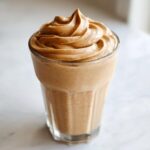A tall glass filled with a thick, brown peanut butter banana smoothie, topped with a perfect swirl.