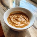 A close-up of thick, creamy peanut sauce swirled in a small white bowl.