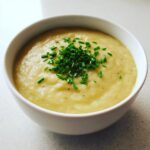 A close-up of a creamy bowl of potato leek soup garnished generously with fresh chopped chives.