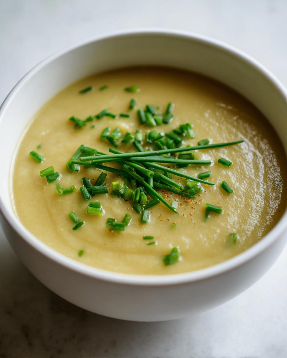 Close-up of a bowl of creamy potato leek soup garnished generously with fresh, chopped chives.