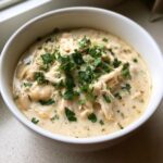 A close-up of a bowl of creamy white chicken chili, topped generously with fresh chopped parsley.