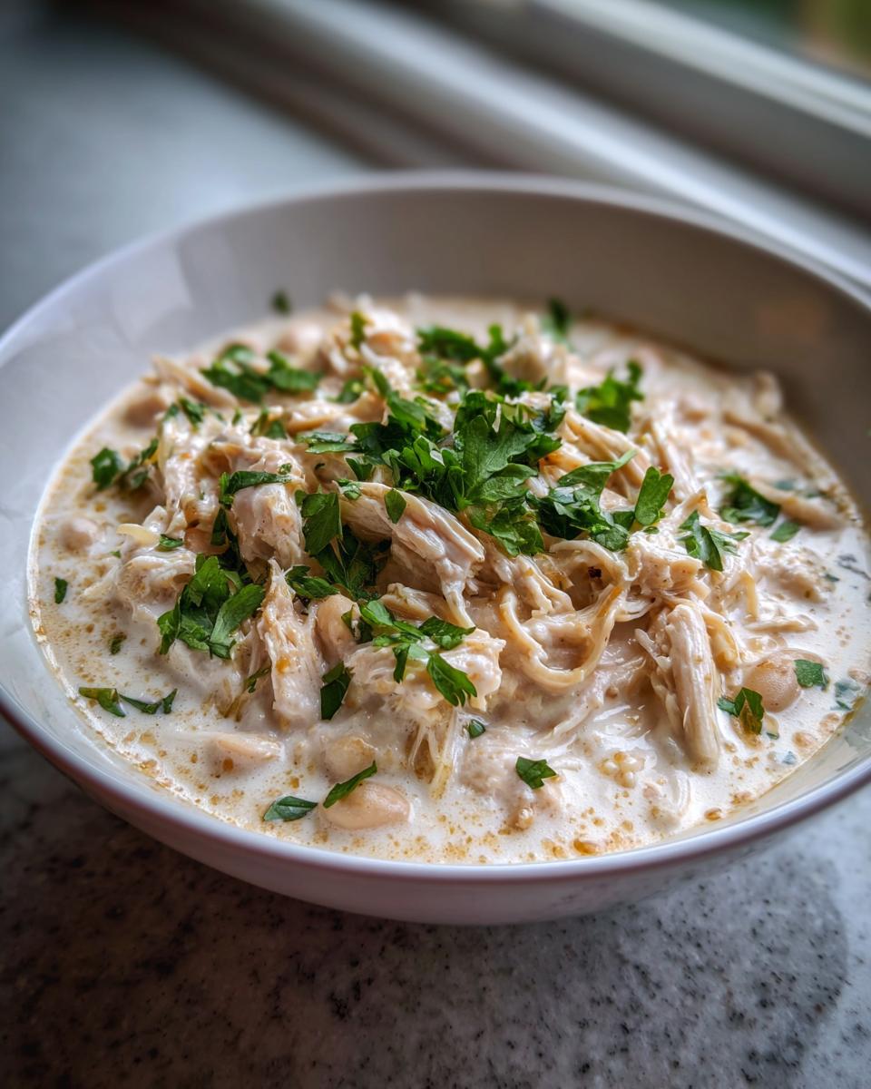 Close-up of a creamy white chicken chili, featuring shredded chicken and white beans, topped with fresh parsley.