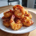 A close-up of golden brown, crispy fried shrimp piled high on a white plate, showcasing the crunchy coating.