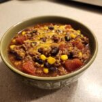 A close-up of a hearty bowl of crockpot cowboy soup, featuring ground beef, black beans, corn, and topped with melted cheddar cheese.