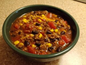 Close-up of a hearty serving of crockpot cowboy soup featuring ground beef, black beans, corn, and tomatoes in a dark green bowl.