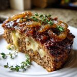 A thick slice of crockpot french onion meatloaf, oozing melted cheese, topped with caramelized onions and fresh thyme.