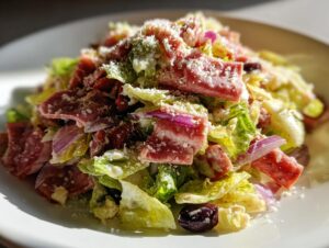 A vibrant, close-up shot of a delicious grinder salad featuring lettuce, sliced cured meats, red onion, and grated cheese.