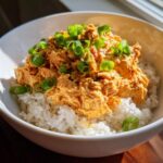 A close-up of creamy, orange-colored tuna rice mixture served over white rice and topped with fresh green onions.