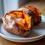Close-up of two baked sweet potatoes, split open to show fluffy orange flesh topped with coarse sea salt.