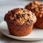 Close-up of a fluffy banana chocolate chip muffin with a golden-brown top studded with melted chocolate chunks.