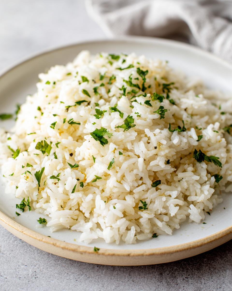 Close-up of fluffy white garlic butter rice garnished generously with fresh chopped parsley on a light plate.