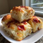 Four fluffy, golden-brown pizza sliders stacked on a white plate, topped with melted cheese and pepperoni pieces.