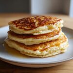 A stack of three fluffy sourdough discard pancakes drizzled with syrup on a light-colored plate.