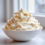 A generous mound of light, fluffy vanilla buttercream frosting piped high in a white bowl.