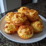A stack of golden-brown, puffy Brazilian cheese bread rolls served on a white plate.