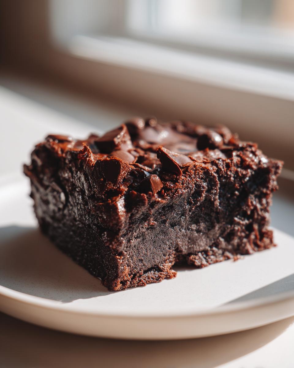 A single, rich, dark chocolate slice of sweet potato brownies topped with melted chocolate chips, sitting on a white plate.