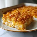 A close-up of a creamy slice of funeral potatoes recipe topped with crunchy, golden corn flakes.
