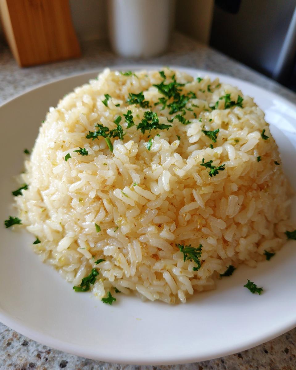 A perfectly molded mound of glossy garlic butter rice topped with fresh chopped parsley on a white plate.