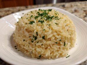 A perfectly molded serving of glistening garlic butter rice topped with fresh chopped parsley on a white plate.