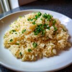 A close-up of fluffy garlic butter rice served on a white plate and topped with fresh chopped parsley.