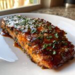 A perfectly baked salmon fillet covered in a shiny, dark glaze and sprinkled with fresh chopped parsley.