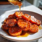 A spoonful of thick, amber glaze is drizzled over a plate of glistening southern candied yams slices.