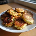 A plate piled high with freshly pan-fried mashed potato cakes, golden brown and sprinkled with chives.