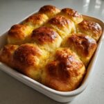 A close-up of golden brown sourdough discard rolls baked together in a white ceramic dish.