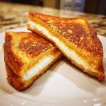 Two halves of perfectly golden brown stuffed french toast, showing a thick layer of white cream cheese filling inside.