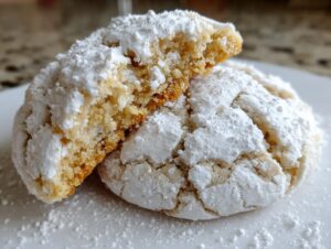 Two gooey butter cookies dusted heavily with powdered sugar, one broken open to show the soft, golden interior.