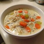 Close-up of a creamy, hearty rice soup filled with shredded chicken, bright orange carrots, and celery pieces.