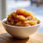 A close-up of chunky, spiced homemade applesauce piled high in a small white bowl.