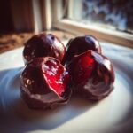 Four homemade chocolate covered cherries on a white plate, two showing the bright red, juicy interior.