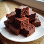 A tempting pile of rich, dark chocolate fudge squares stacked on a small white plate.