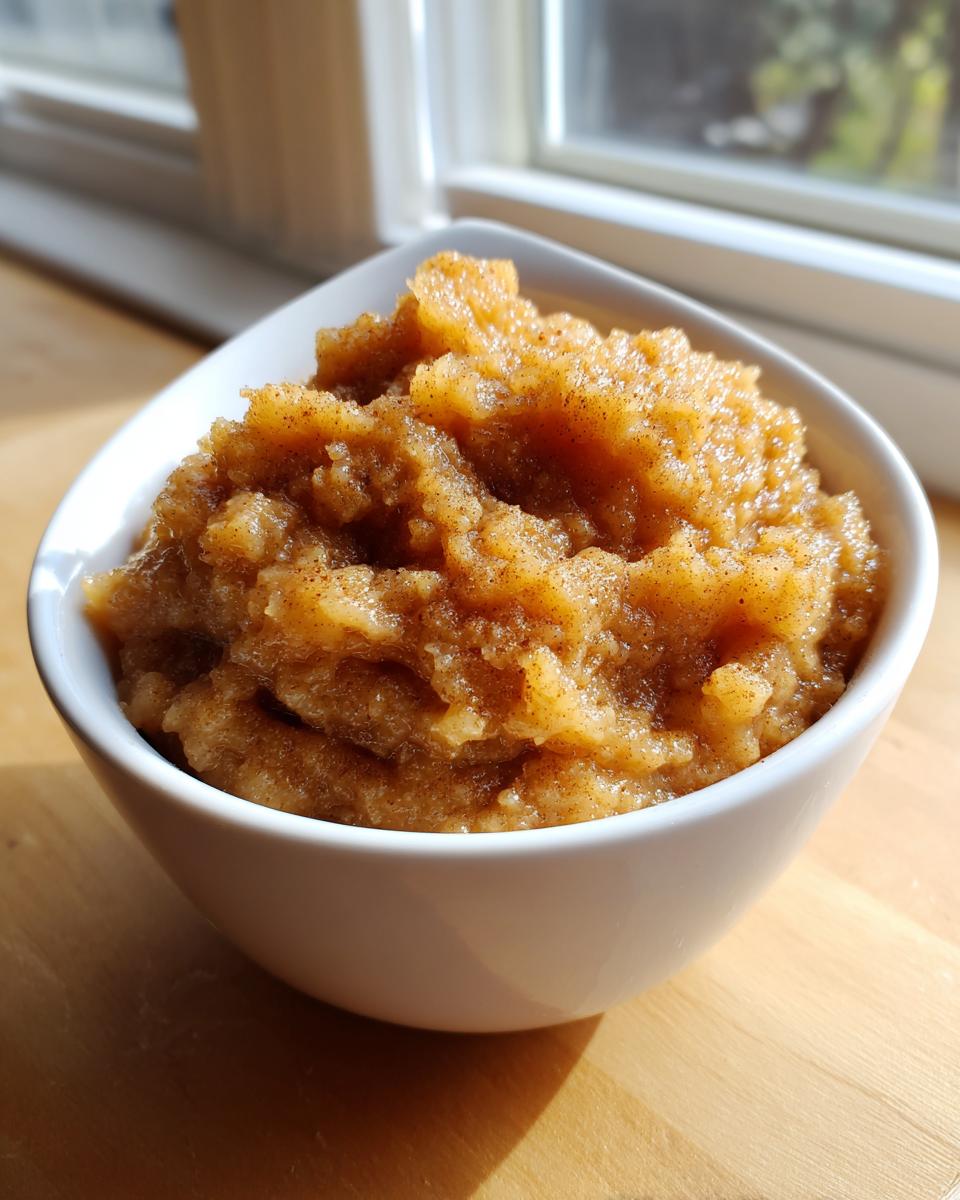 Close-up of homemade applesauce, spiced with cinnamon, served in a white bowl near a window.