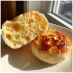 A homemade English muffin split open showing the signature nooks and crannies texture inside, next to the toasted exterior.