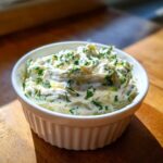 A close-up of creamy, homemade tartar sauce recipe topped generously with fresh chopped green herbs in a white bowl.