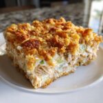A square serving of creamy hot chicken salad with a crunchy, golden-brown topping on a white plate.