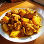 A close-up of flavorful Jamaican curry chicken pieces mixed with large chunks of potato in a rich yellow sauce.