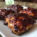 Close-up of four pieces of juicy bbq chicken thighs coated in thick, shiny barbecue sauce.