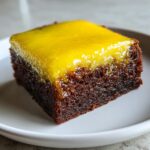 A square slice of rich, dark chocolate lemon brownies topped with a thick, glossy, bright yellow lemon glaze.