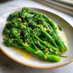 Close-up of vibrant green broccolini stalks tossed in lemon butter sauce and topped with lemon zest.