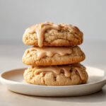 Three stacked maple cookies topped generously with dripping brown butter icing on a small plate.