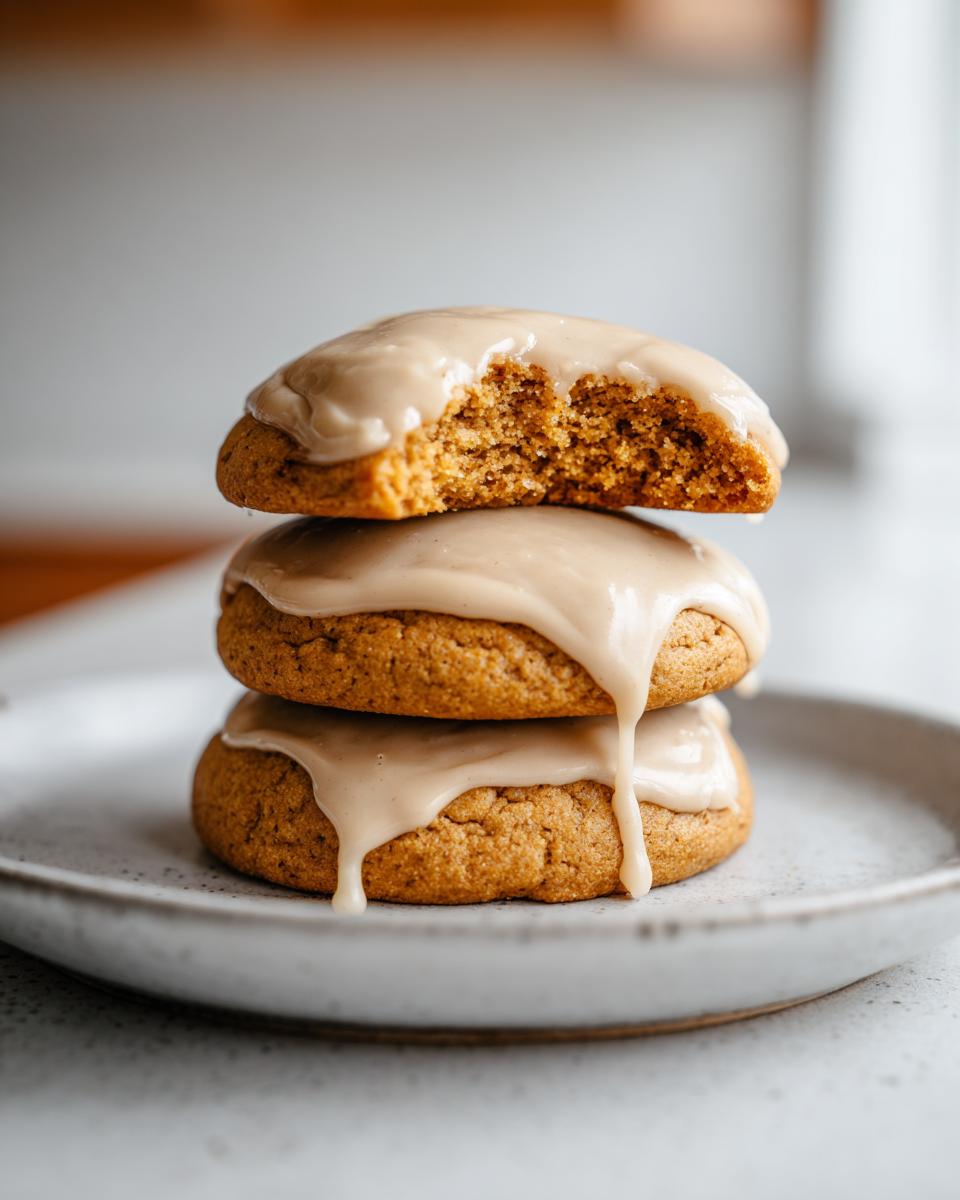 A stack of three soft maple cookies topped with dripping brown butter icing, one cookie is broken open.